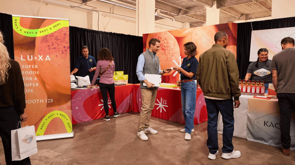 Tradeshow booth with participants testing product samples and receiving event materials.